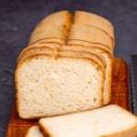 sliced loaf of gluten free sourdough bread on brown wood board with knife cuts