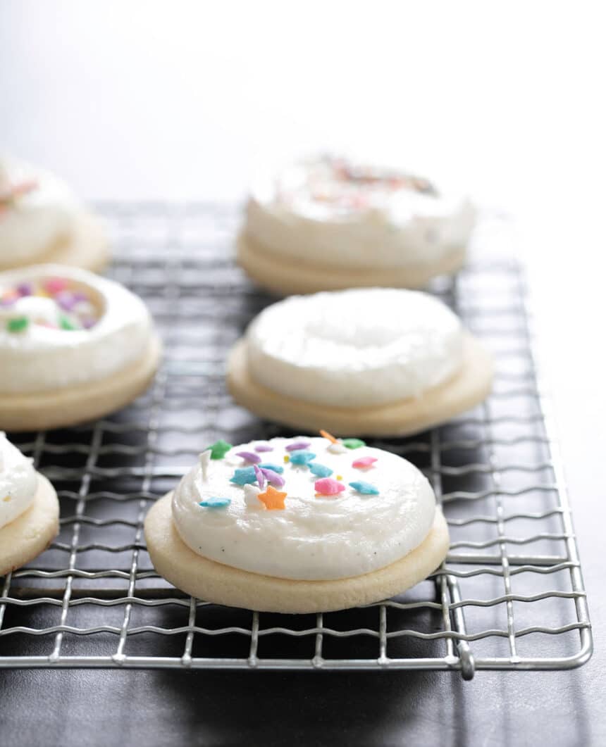 Gluten free sugar cookies decorated with frosting and sprinkles, sitting on rack