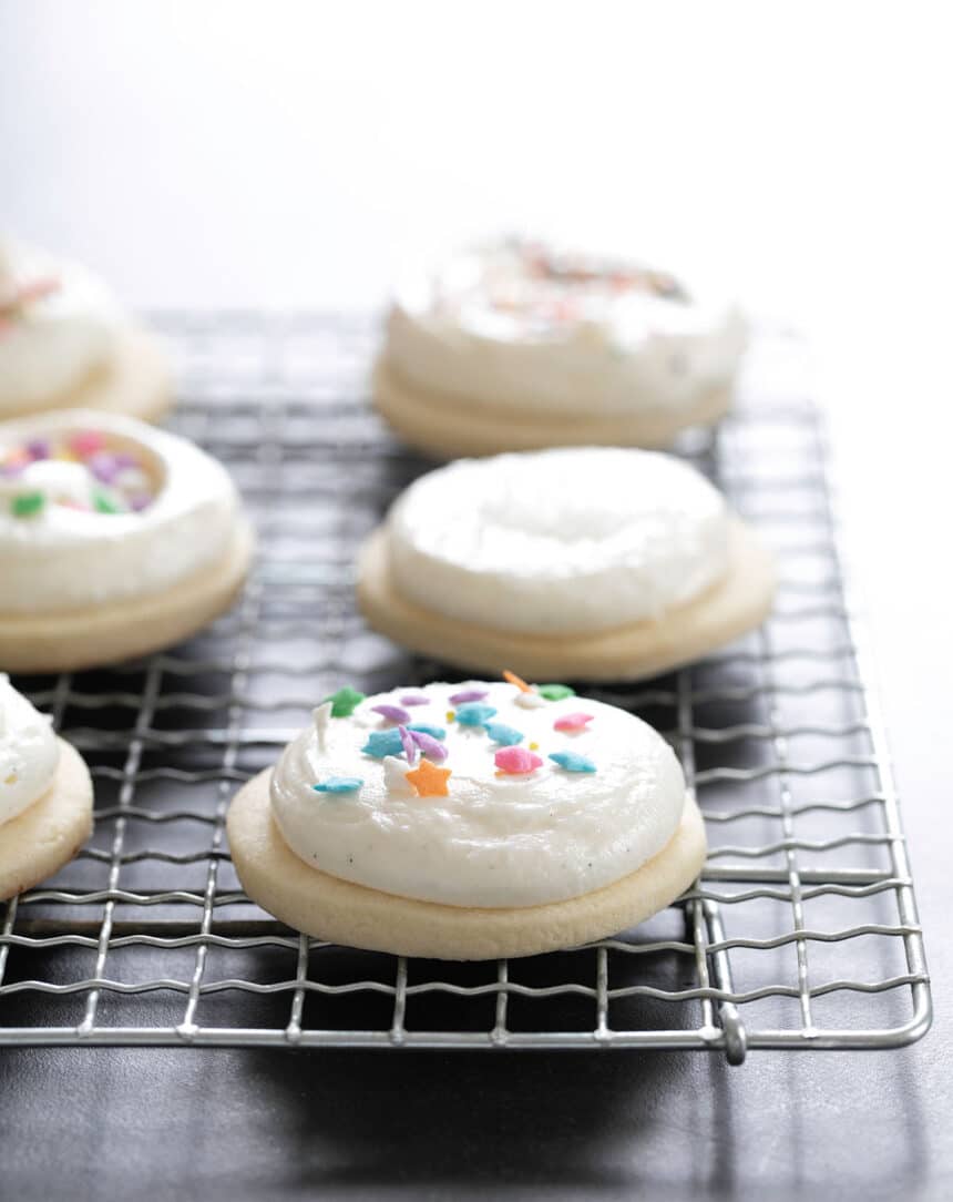 Gluten free sugar cookies decorated with frosting and sprinkles, sitting on rack