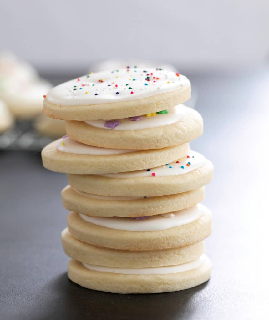 Eight round sugar cookies with white frosting in a vertical stack