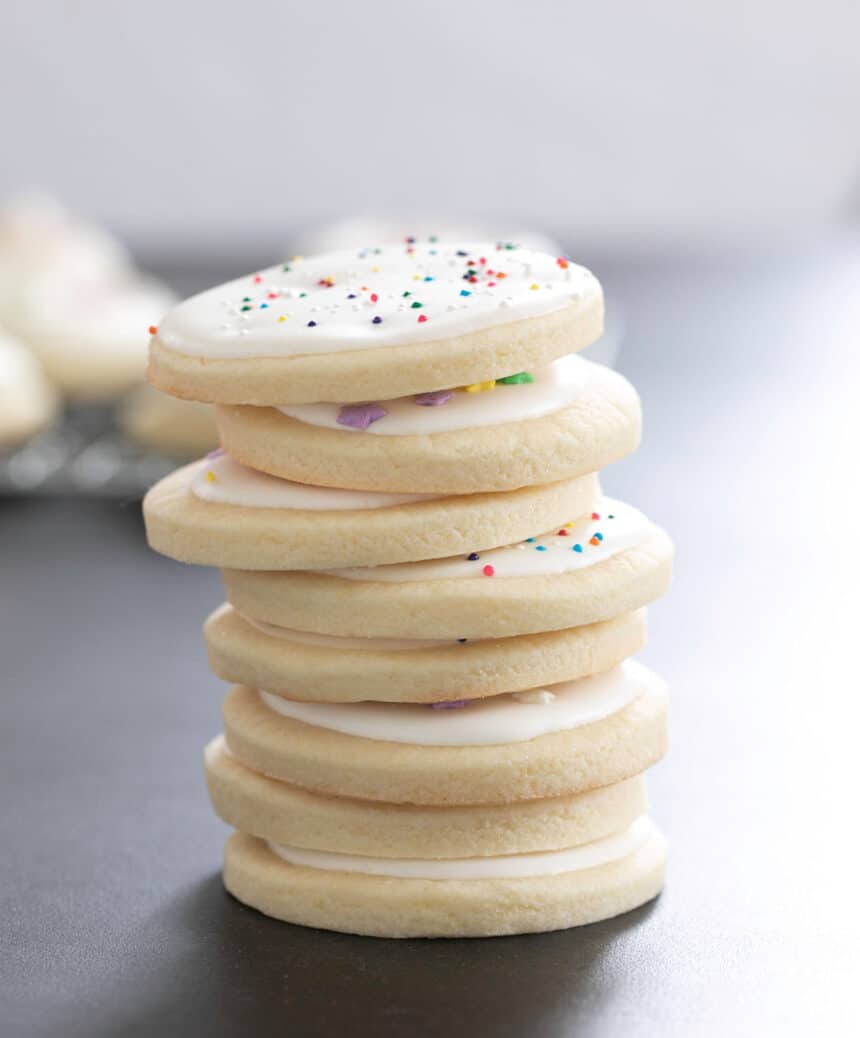 Eight round sugar cookies with white frosting in a vertical stack