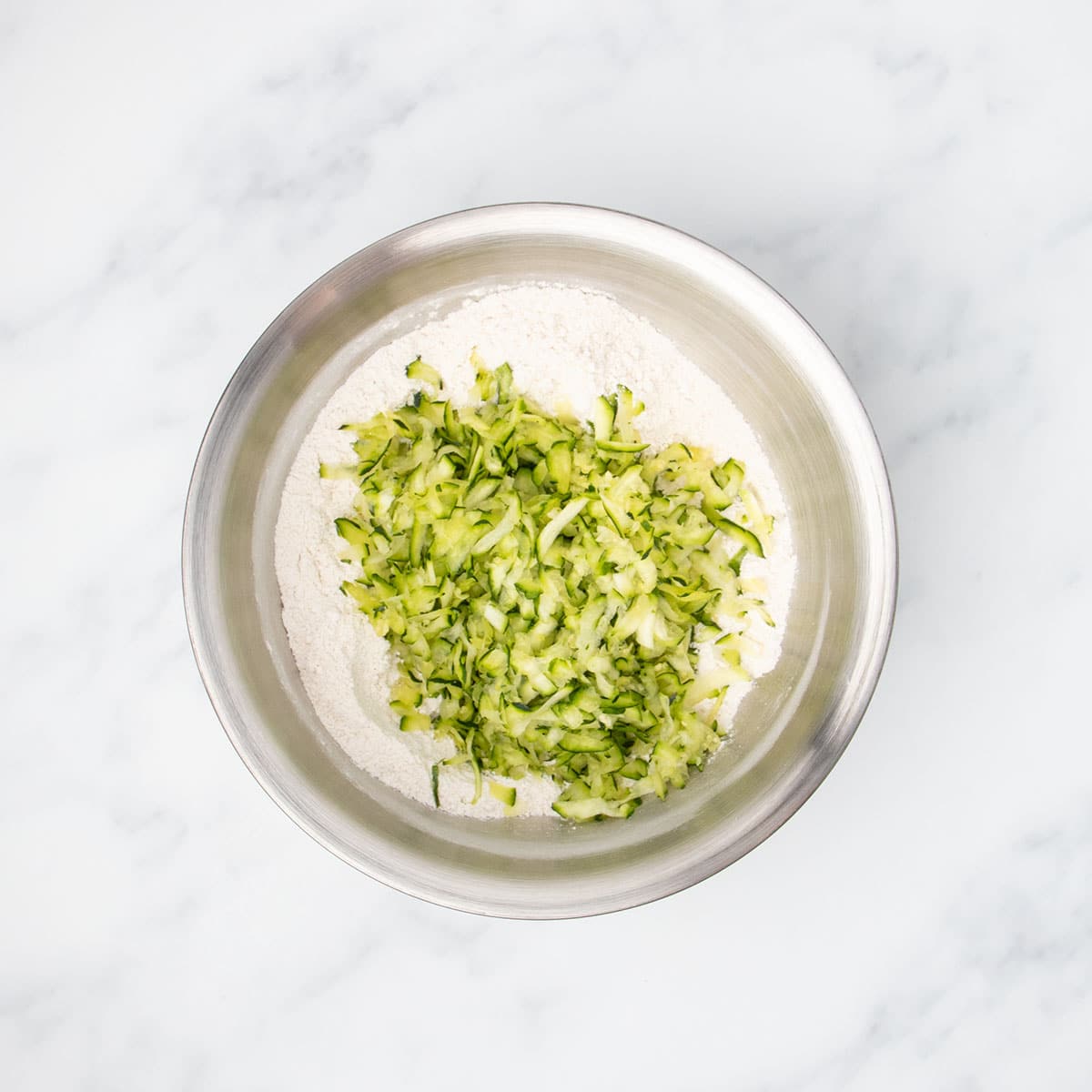 Same bowl with white flour mixture with green shredded zucchini on top.
