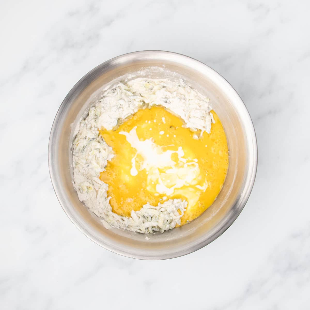 Yellow beaten eggs and white buttermilk on top of flour mixture in mixing bowl.