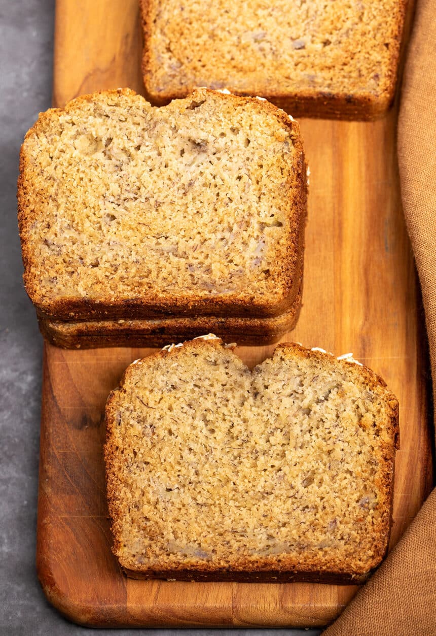 overhead image of 4 slices of oat flour banana bread on brown wood paddle board with brown cloth