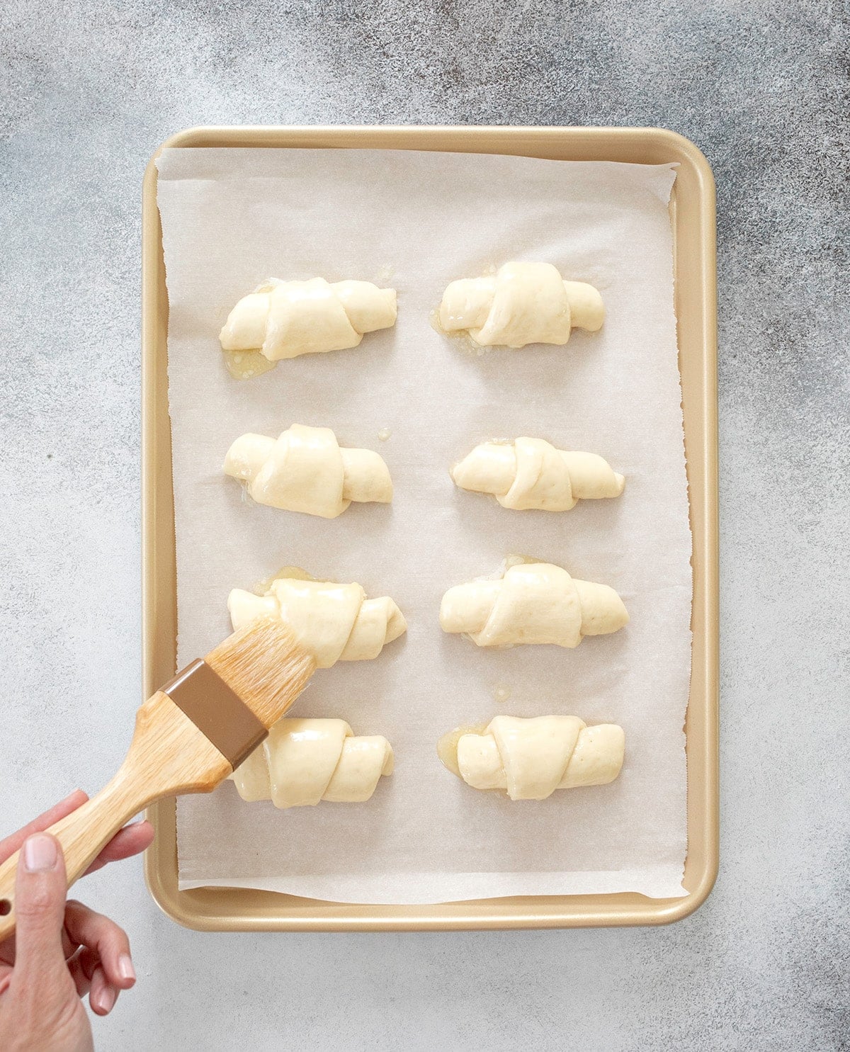 Hand holding a brush that is brushing gluten free crescent rolls with melted butter