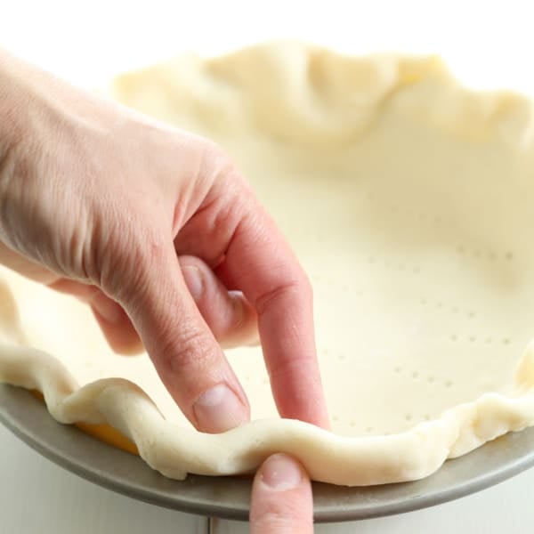 closeup of fingers crimping edge of raw gluten free pie crust in metal pie plate