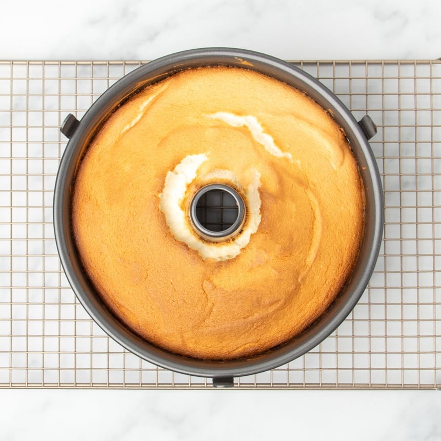 light brown baked angel food cake in tube pan on gold colored wire rack
