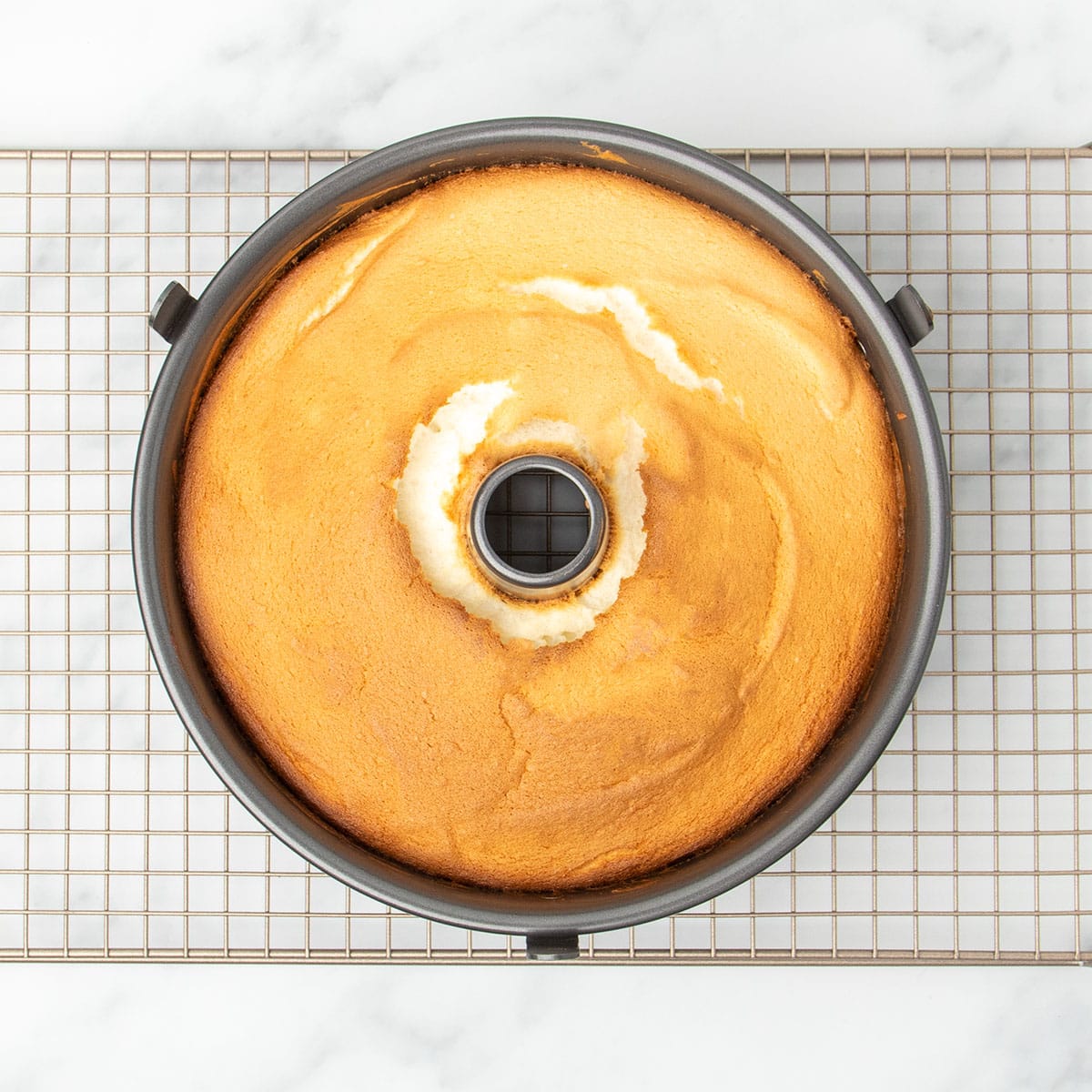 light brown baked angel food cake in tube pan on gold colored wire rack