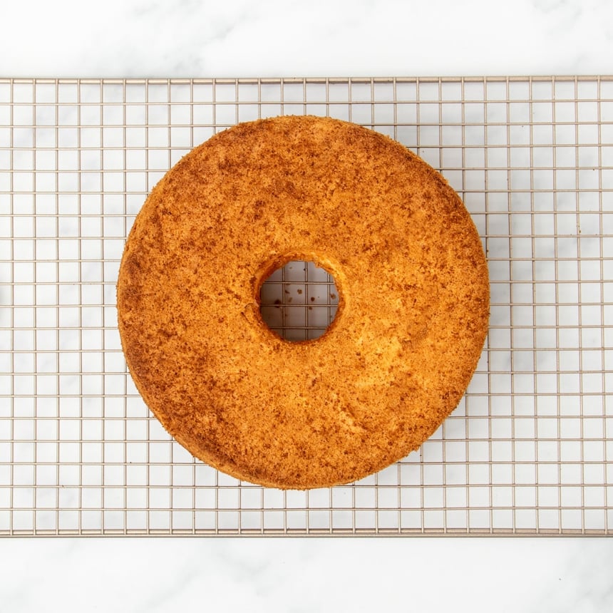 whole golden brown angel food cake on gold colored wire rack