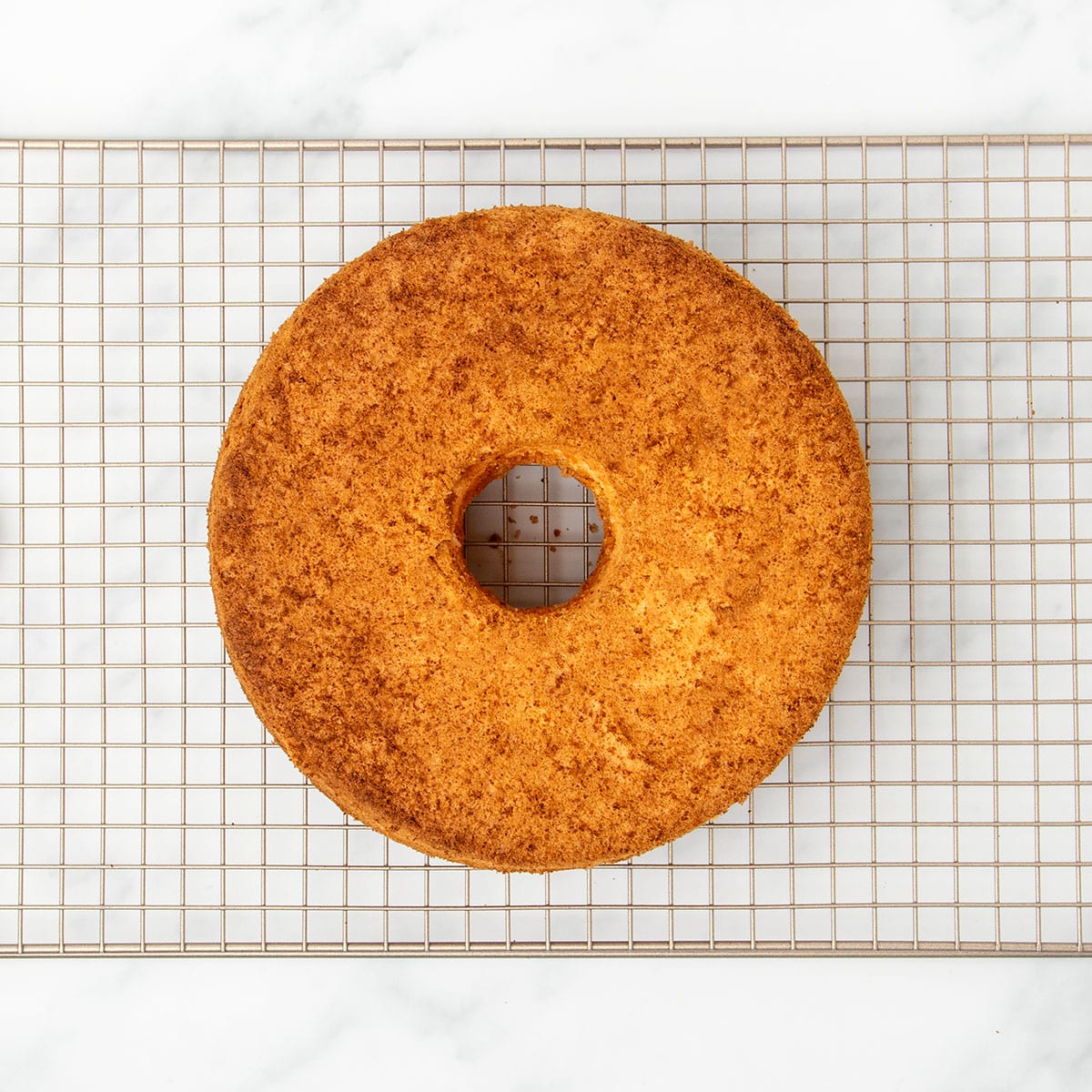 whole golden brown angel food cake on gold colored wire rack