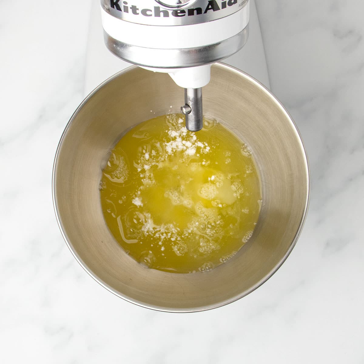 white stand mixer with round metal mixing bowl with egg whites and cream of tartar