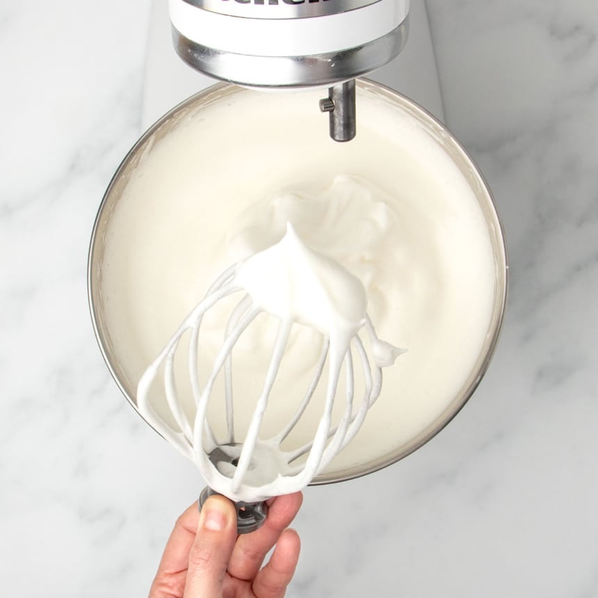 white raw meringue in mixing bowl with stiff peaks of meringue on wire whisk