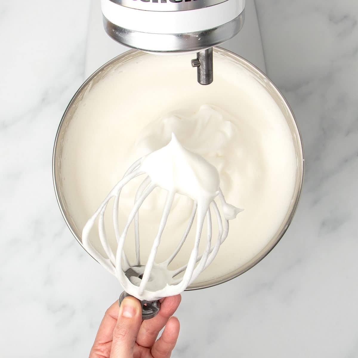white raw meringue in mixing bowl with stiff peaks of meringue on wire whisk
