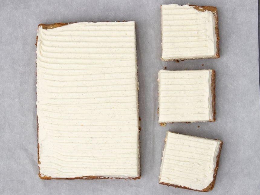 Square banana cake with top covered with white cream icing with 3 cut squares, all on white paper