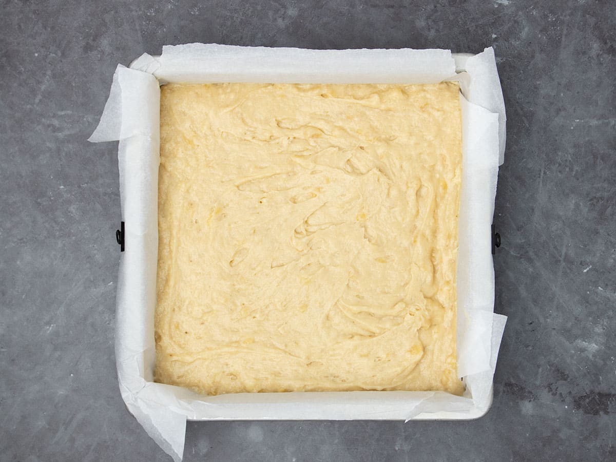 light yellow batter in square baking pan lined with white parchment paper