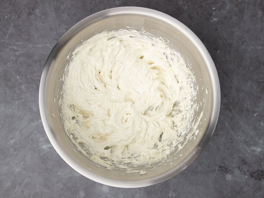 Large bowl of round metal mixing with white cheese icing mounted with black vanilla seed machines