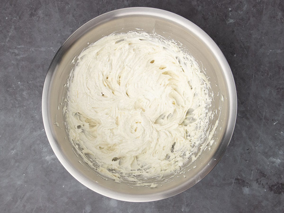 large round metal mixing bowl with whipped white cream cheese frosting with black flecks from vanilla seeds
