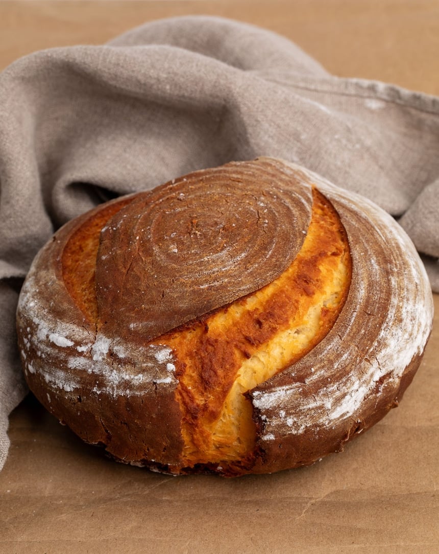 round brown boulé loaf of bread with two slashes on the top on brown kraft paper with tan cloth