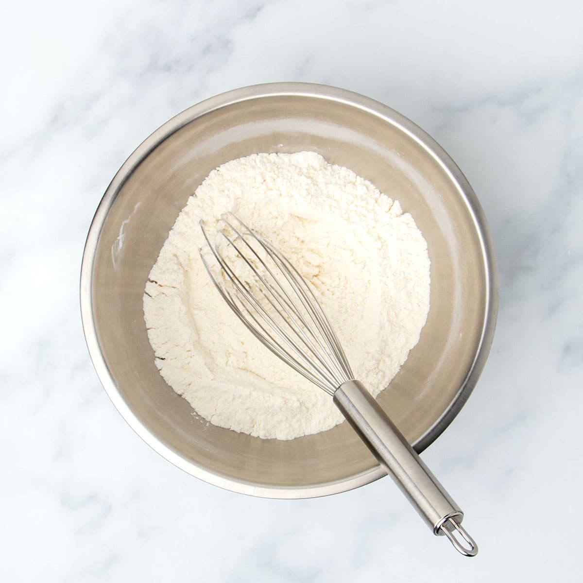 same bowl with pale white-tan powder whisked together with large metal wire whisk