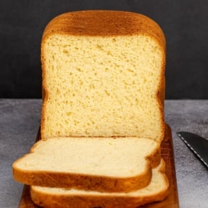 Yellow sliced bread with brown crust on brown cutting board