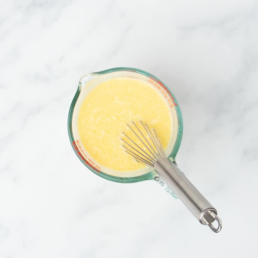 2 cup glass measuring cup with yellow whisked mixture and metal wire whisk in cup