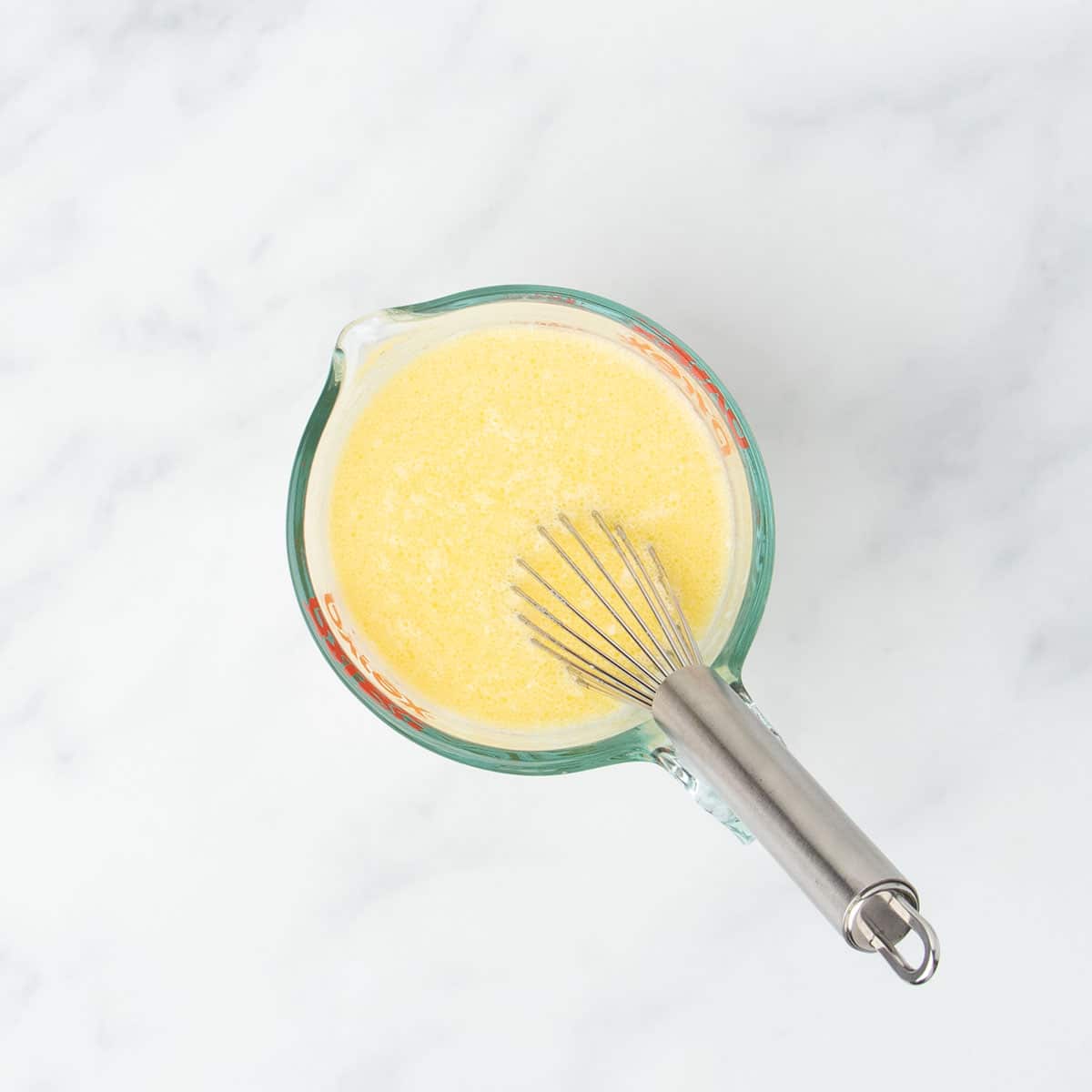 2 cup glass measuring cup with yellow whisked mixture and metal wire whisk in cup