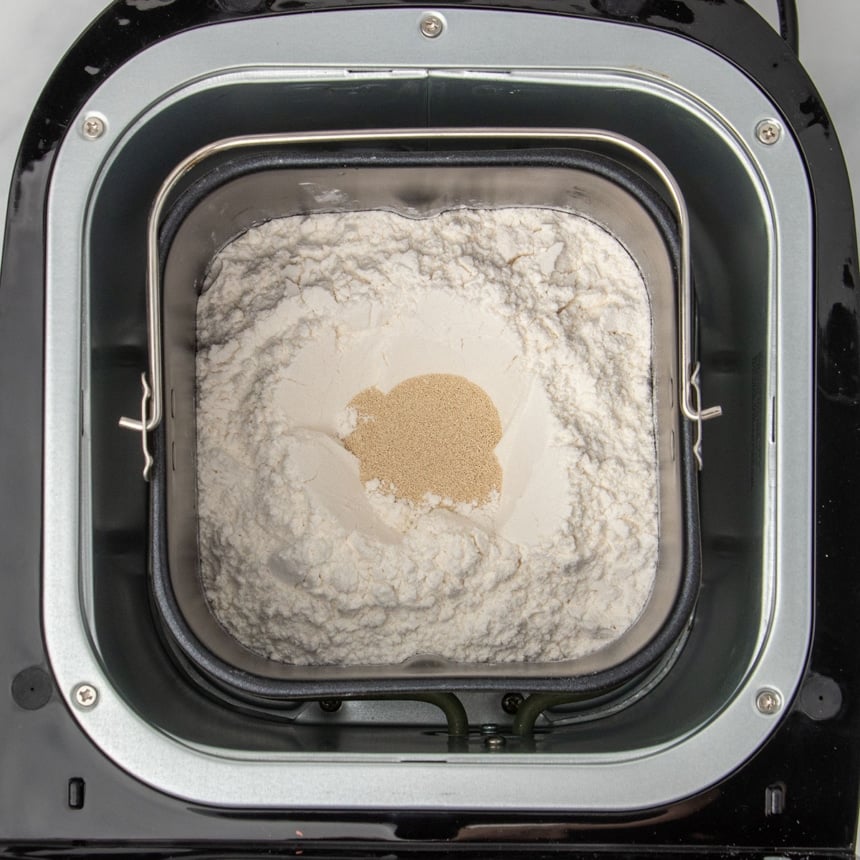 same baking pan with flour on top and instant yeast granules in small hole in center of flour in baking pan in bread machine