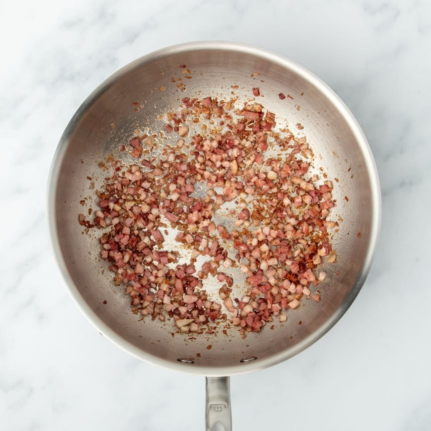 round metal saucier pan with handle with cooked cubed pink and brown pancetta