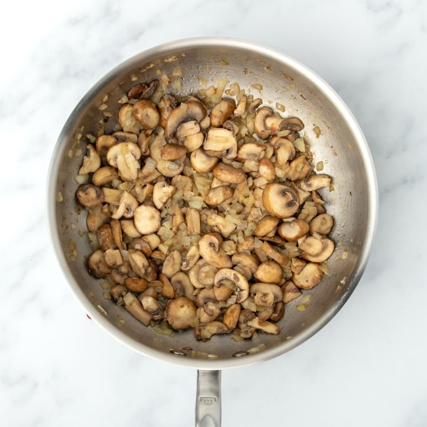 same saucier pan with cooked sliced brown mushrooms and light yellow cooked diced onion
