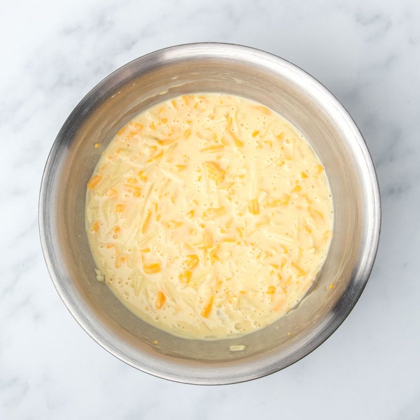 same mixing bowl with yellow shredded cheddar cheese mixed into yellow mixture