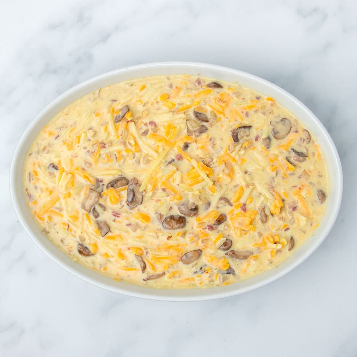 same raw breakfast casserole yellow liquid mixture with brown, yellow and pink pieces now in white oval casserole dish