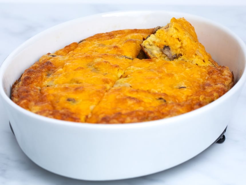 cooked gluten free breakfast casserole in white dish from side showing dish cut into 6 slices and one slice partially on its side revealing cooked brown mushrooms and yellow eggs inside