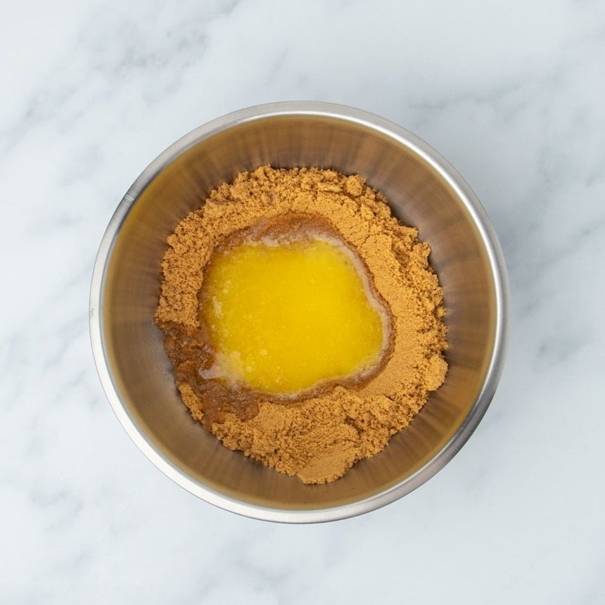 round metal mixing bowl with brown cookie crumbs and yellow melted butter