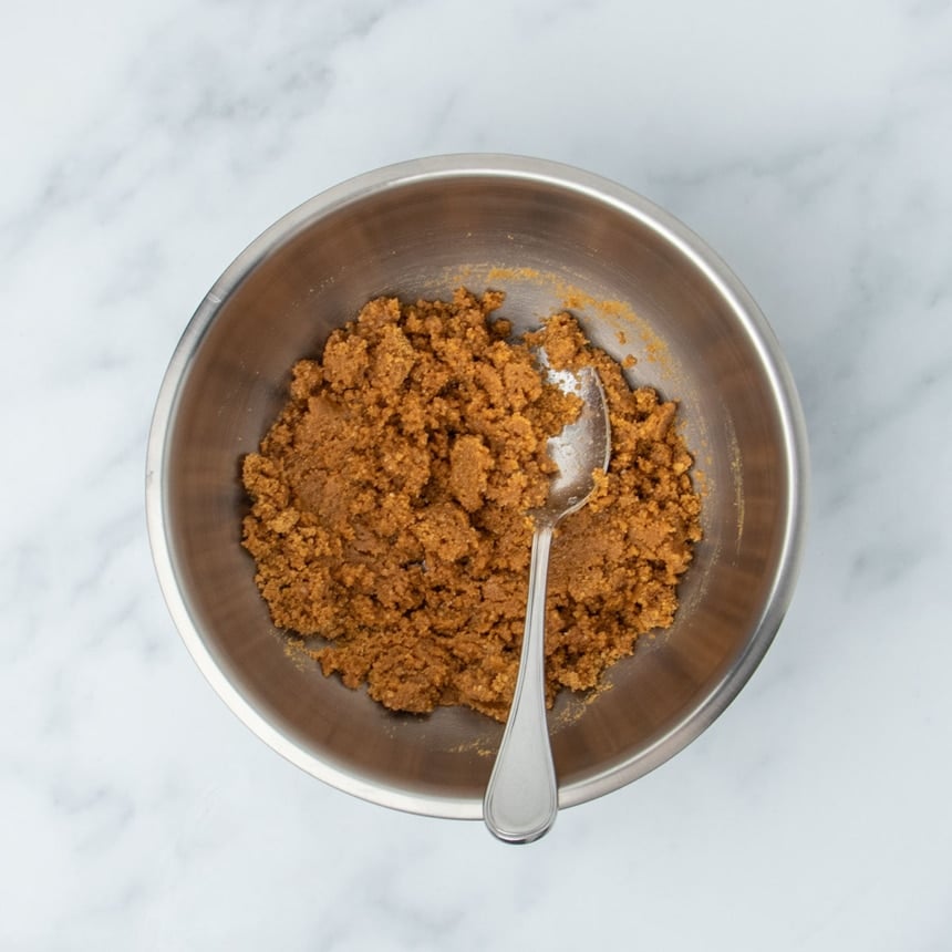 same mixing bowl with ingredients mixed into brown clumps with metal mixing spoon