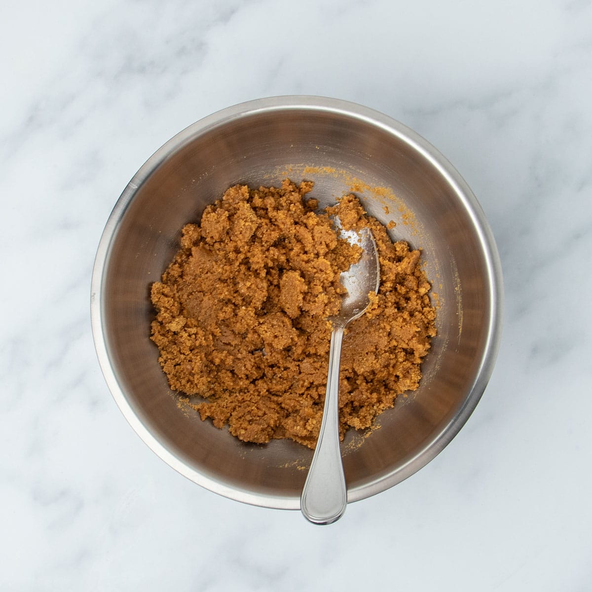 same mixing bowl with ingredients mixed into brown clumps with metal mixing spoon