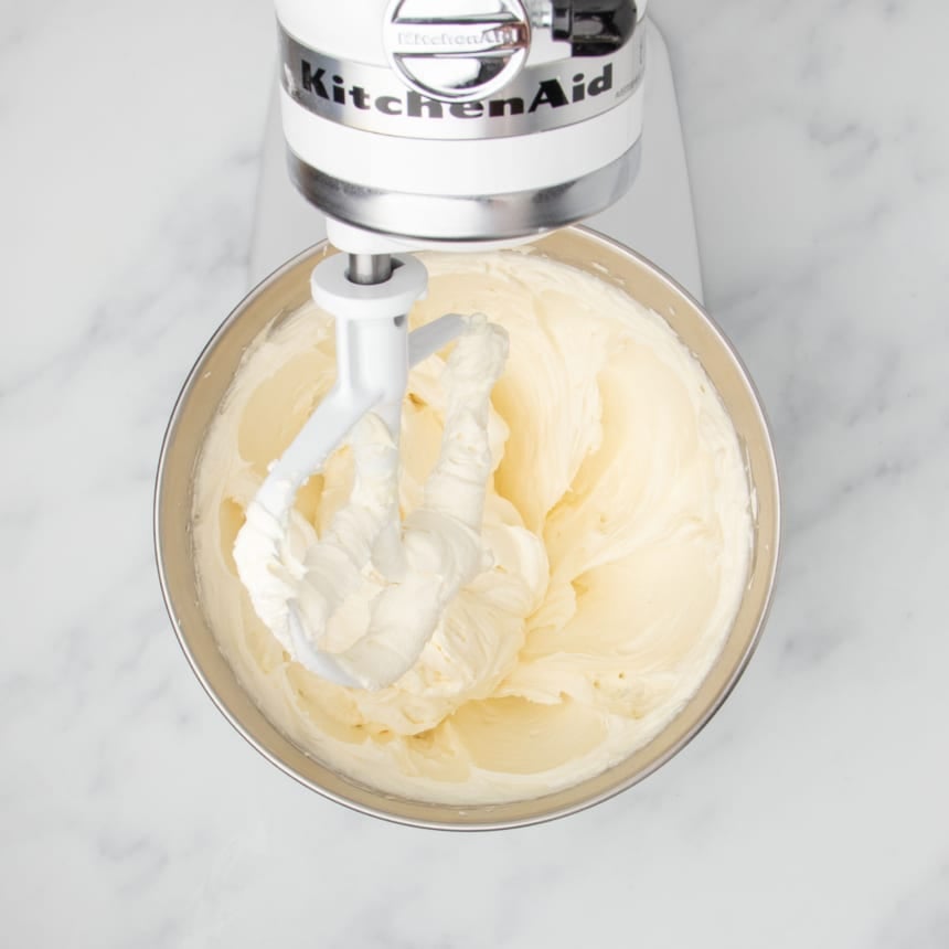same mixing bowl with cream colored fluffy mixture of beaten cream cheese with white paddle attachment and white kitchenaid mixer