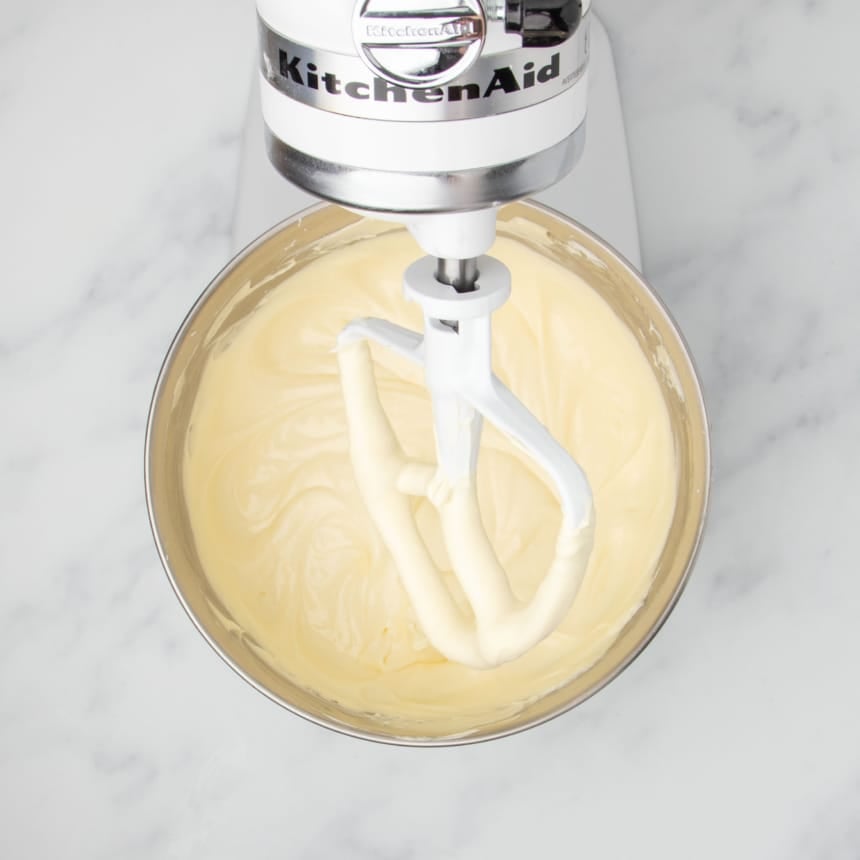 smooth light yellow raw cheesecake mixture in mixing bowl with white paddle