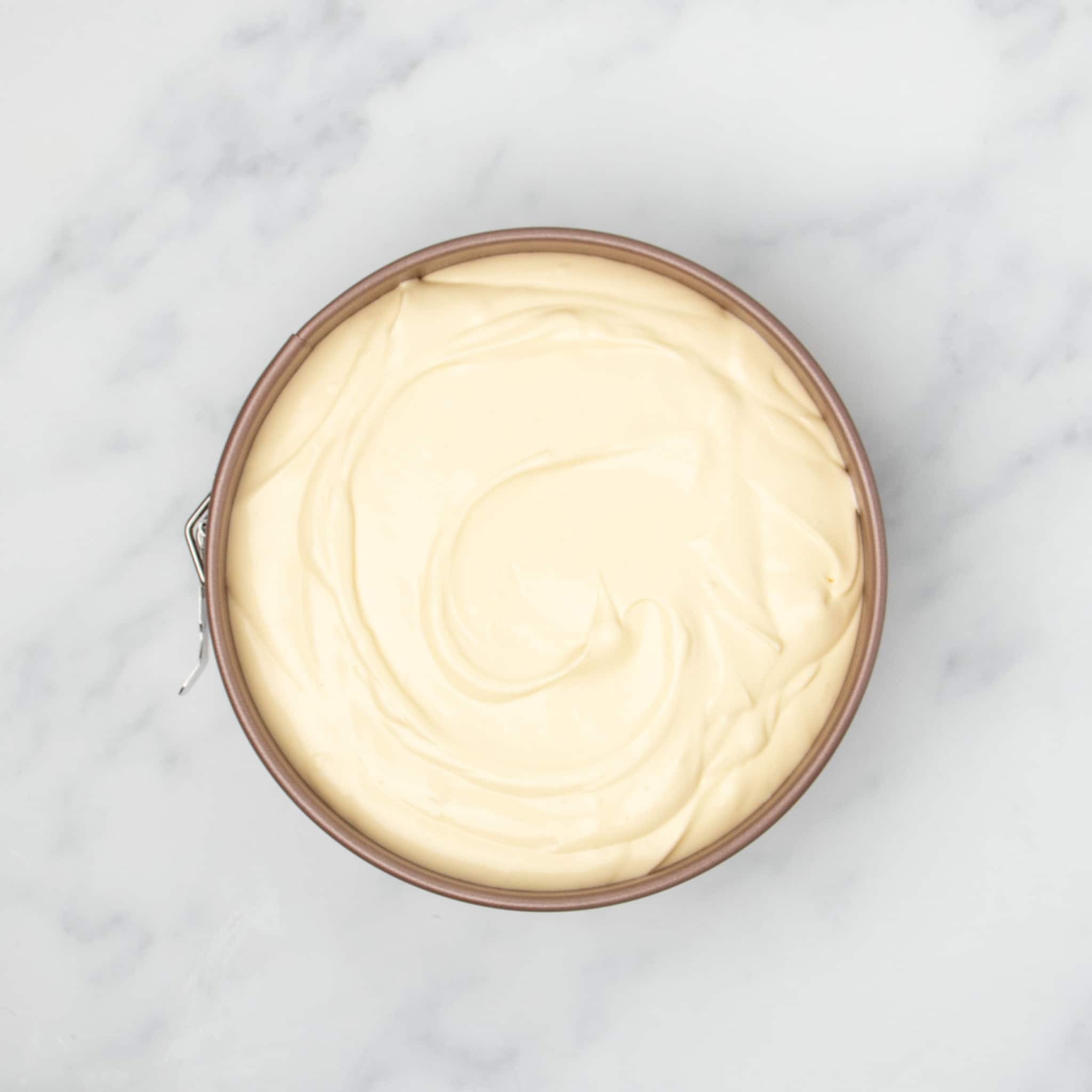 light yellow raw cheesecake mixture in gold colored round springform pan