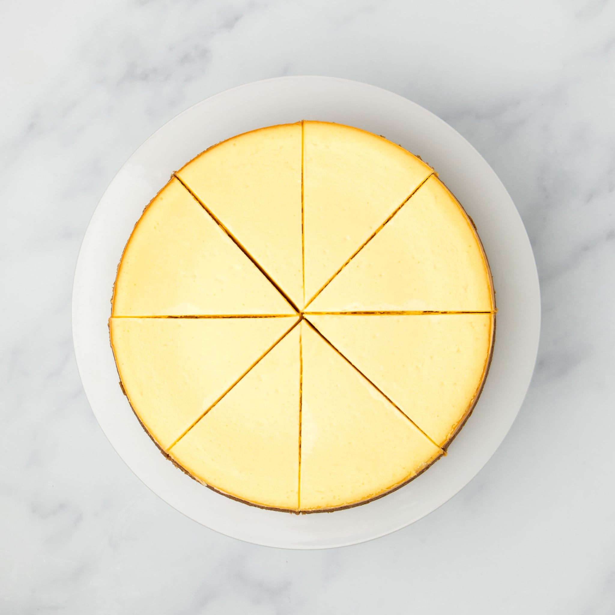 same baked cheesecake out of pan sliced into 8 triangles on a white plate