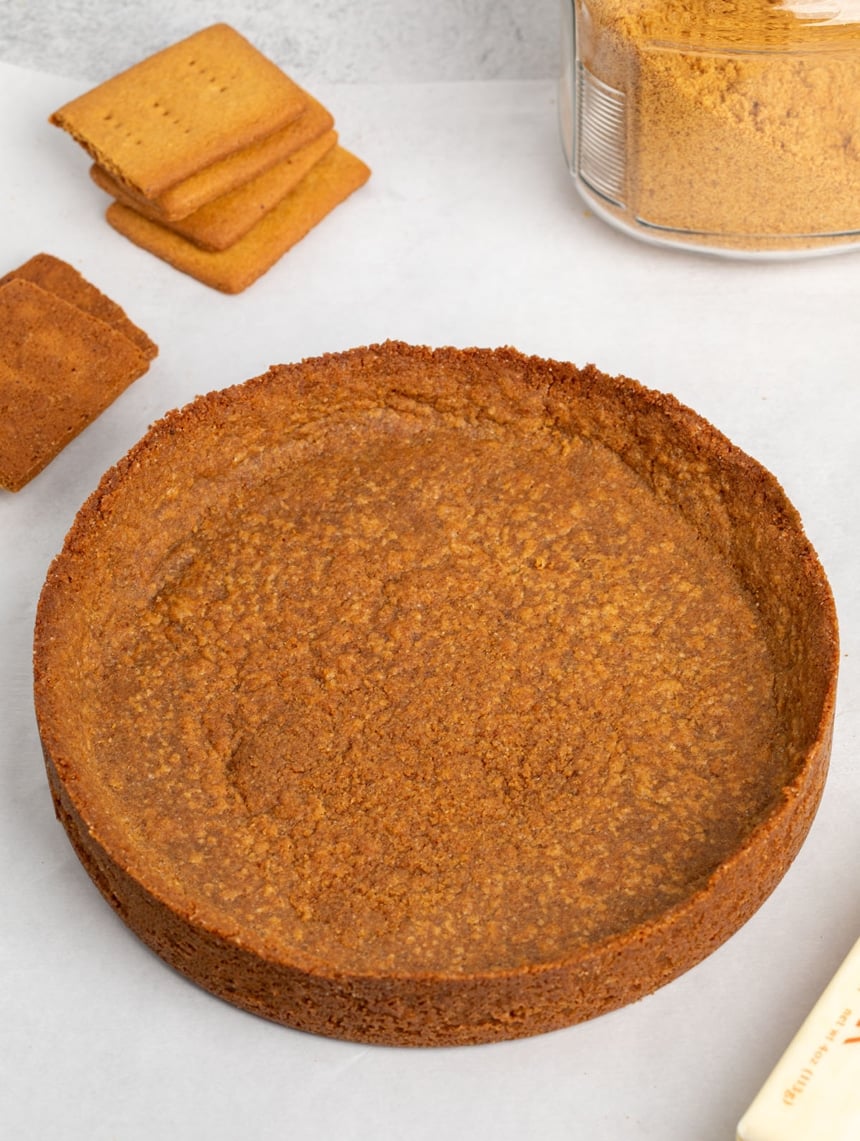 graham cracker crust on white paper with more graham crackers broken in half and a glass jar with brown crumbs inside