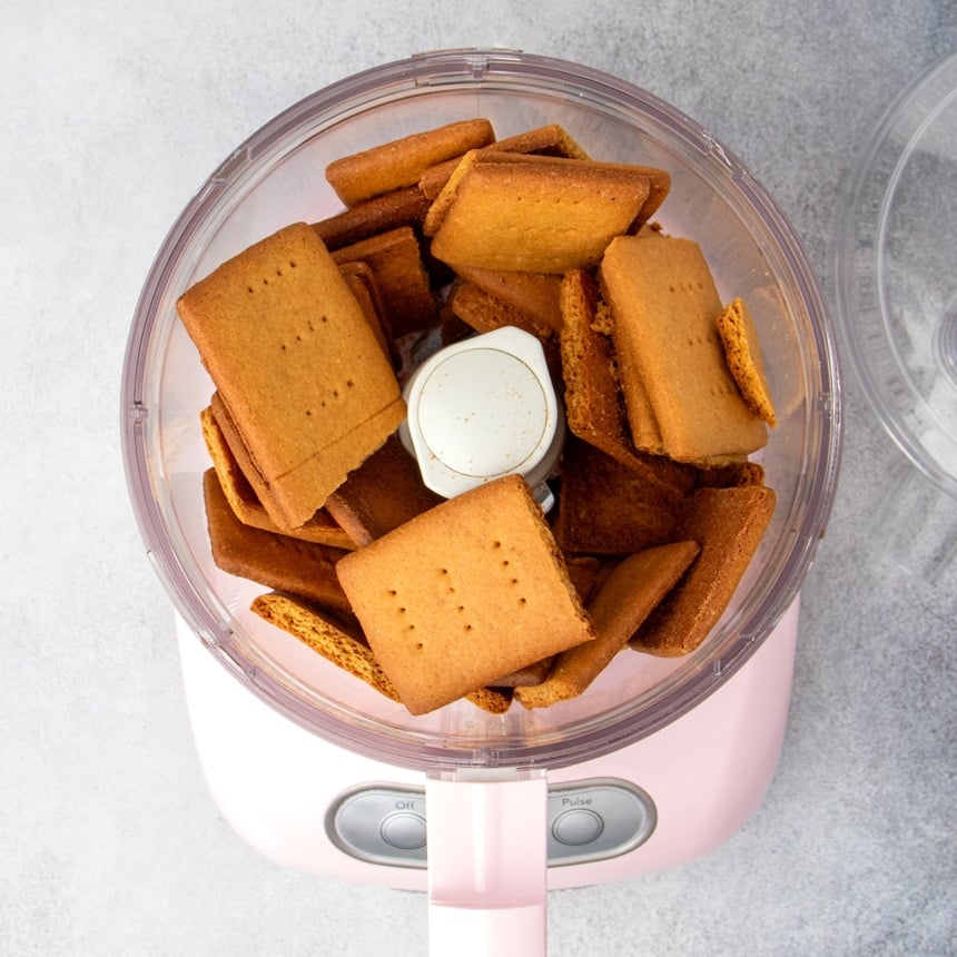 broken brown gluten free graham crackers in pink colored food processor with open top
