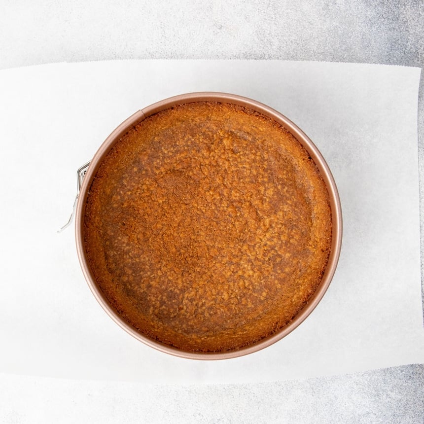 overhead image of baked graham cracker crust in springform pan on white paper