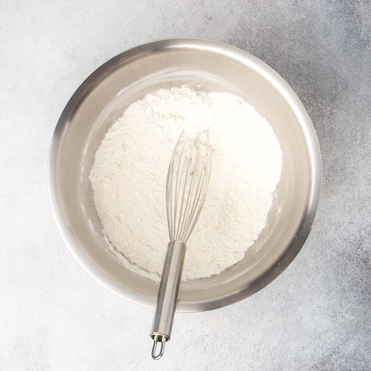 round metal mixing bowl with white flour mixture and metal wire whisk