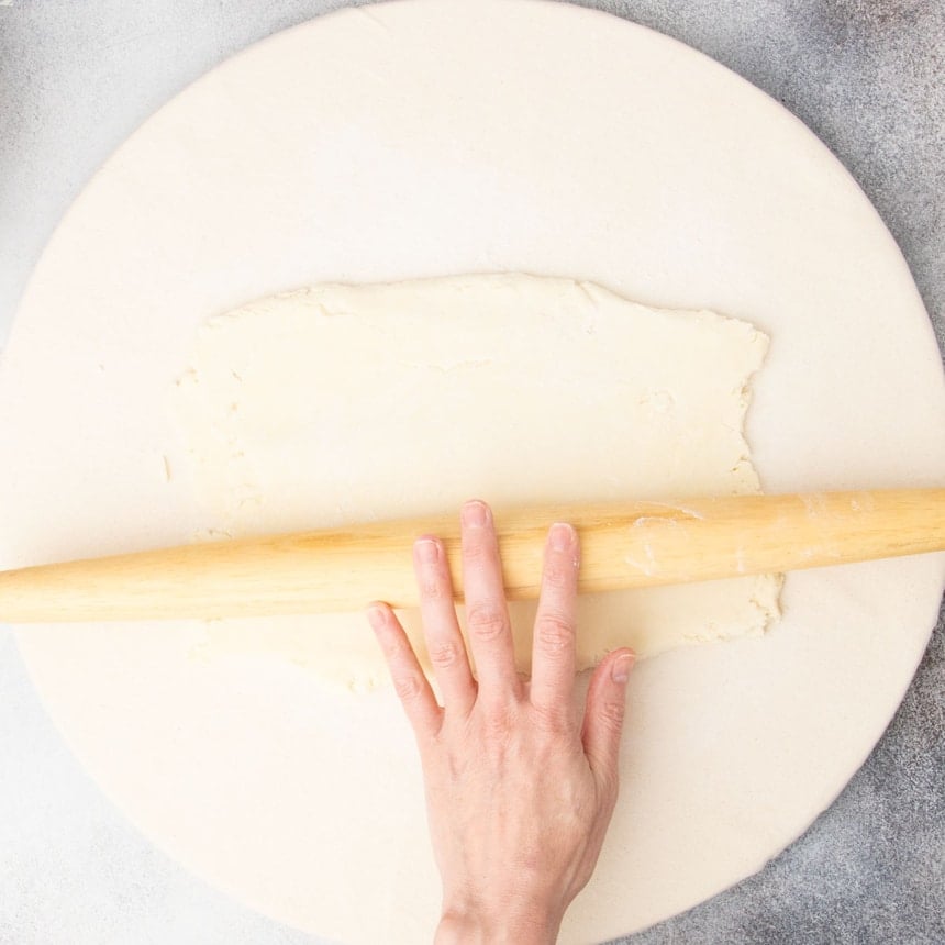 fingers rolling same blonde rolling pin on top of rectangle or raw dough on board