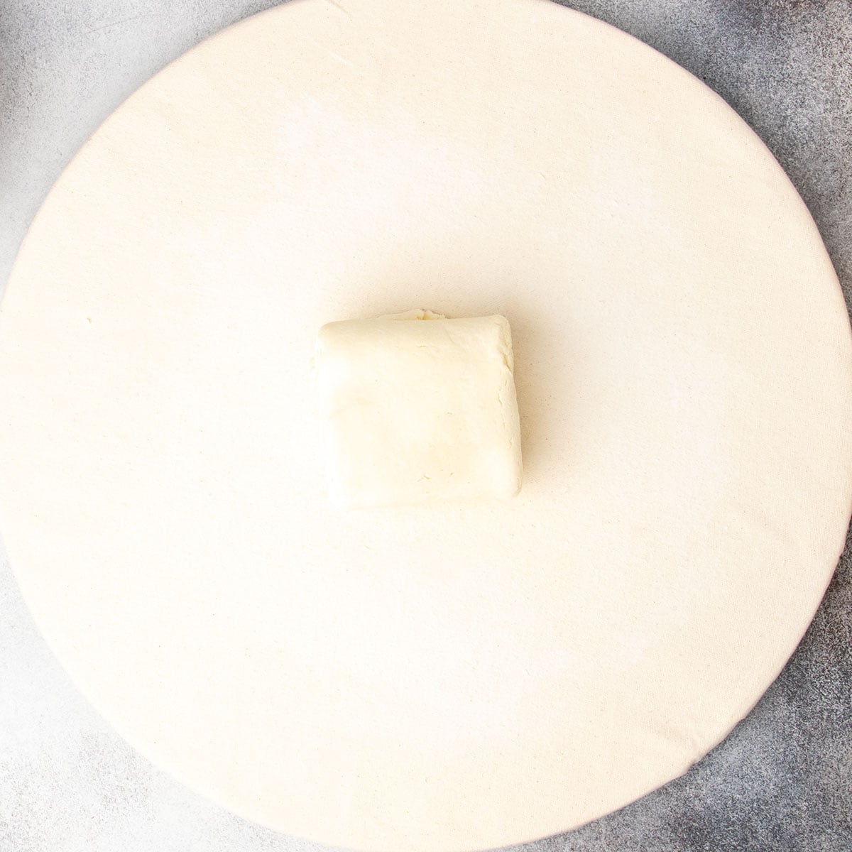 Square of rolled and folded raw dough on pastry board.