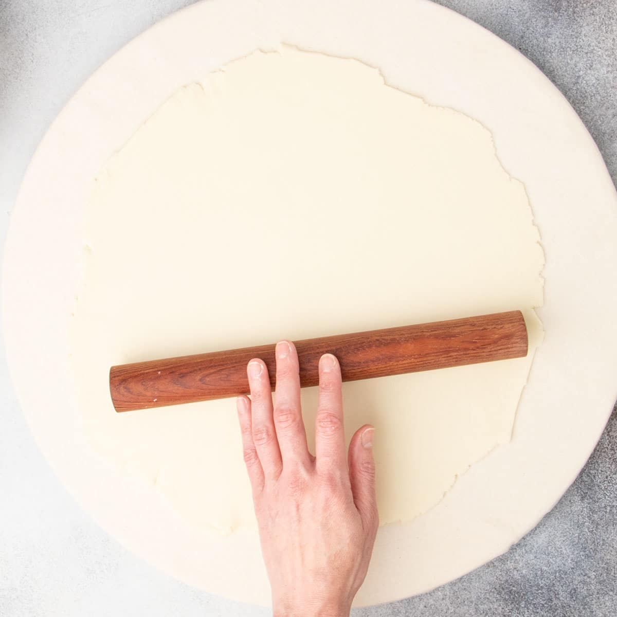 fingers rolling short dark wood rolling pin on 10-inch round raw pie crust on board