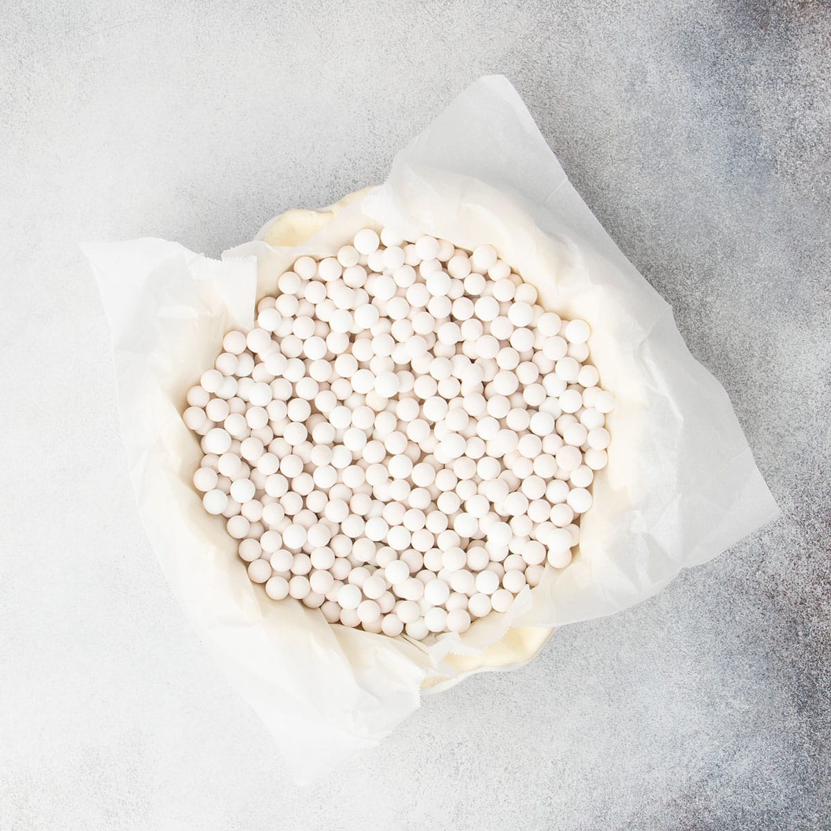 same raw pie crust lined with white paper, which is topped with white round pie weights
