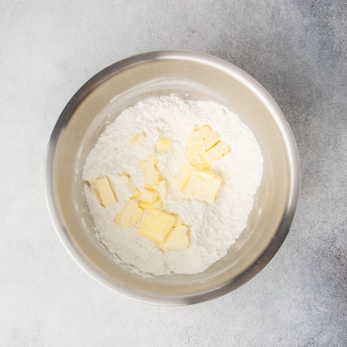same bowl with chopped yellow butter on top of flour mixture