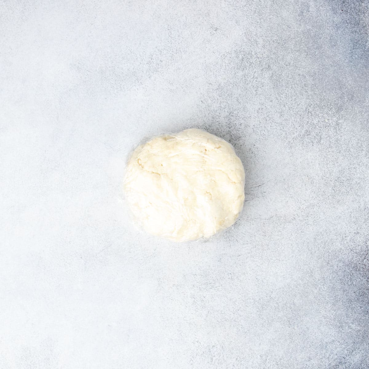 light tan disk of pie crust wrapped in plastic wrap on light gray surface