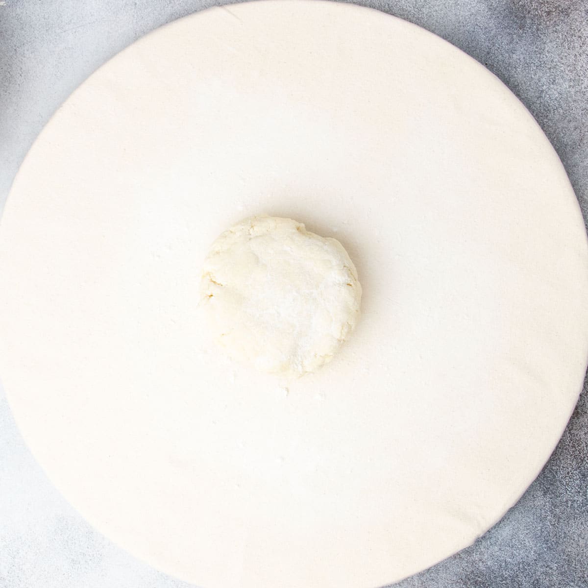 light tan pie crust disk with white flour sprinkled on top sitting on round light canvas board